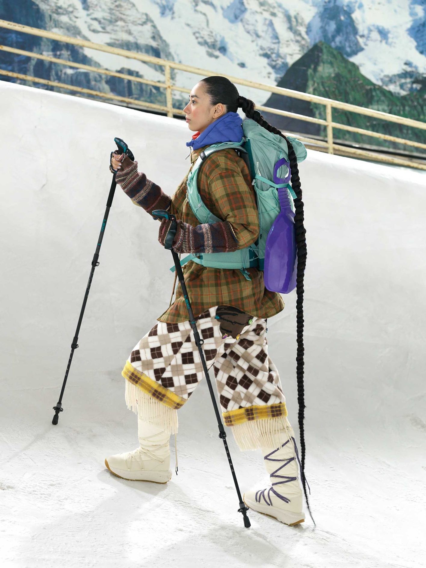 タータンチェック柄やボーダー、アーガイル模様など、同系色のテキスタイルを大胆にミックス。背負ったソリと同じ紫をフードや靴紐など随所にちりばめてアクセントに。ジャケット ¥59,400（スドーク）、パンツ ¥95,700（ペナルティメイト | 共にエムエイティティ）／中に着たダウン ¥25,3 00（マーモット | サードシップ）／中に着たタートルネック ¥20,900（スノーピーク）／バックパック ¥26,400（ミレー | ミレー・マウンテン・グループ・ジャパン・カスタマーサービス）／アームウォーマー ¥24,200（セヴシグ | サカス ピーアール）／スノーブーツ ¥39,600（ハンター | ハンタージャパン カスタマーサービス）／トレッキングポール＊スタイリスト私物